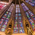 Aachener Dom Blick nach oben entlang der bunten Fenster des Aachener Doms, zwischen denen Säulen mit Statuen stehen.