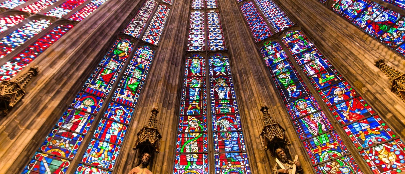 Aachener Dom Blick nach oben entlang der bunten Fenster des Aachener Doms, zwischen denen Säulen mit Statuen stehen.