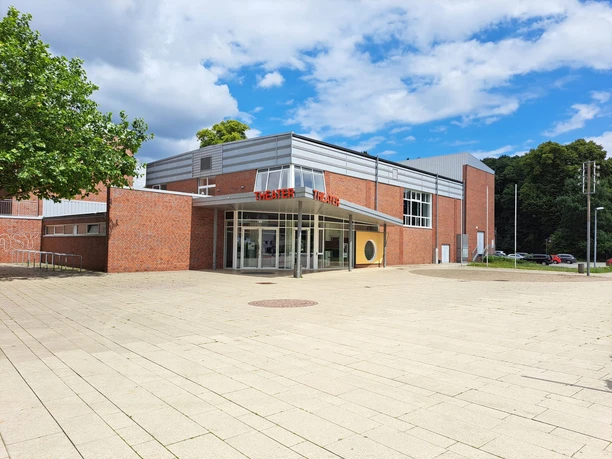Backsteinbau mit moderner Glaseingangsfront des Theaters Meppen unter blauem Himmel mit Wolken.