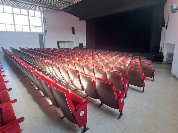 Blick in den Theatersaal mit roten Sitzreihen, moderner Decke und Bühne im Hintergrund