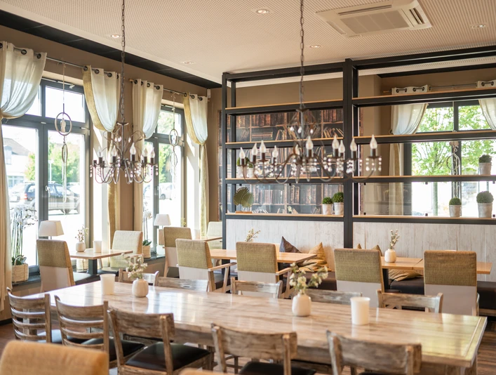 Ferdinands Bäckerei | Restaurant Helle, moderne Innenansicht eines Restaurants mit großen Fenstern, Holztischen und eleganter Beleuchtung.