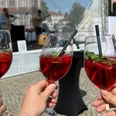 Weinfest_Weingläser.jpeg 3 Menschen halten Weingläser mit roten Getränken. Im Hintergrund spielen Musiker.