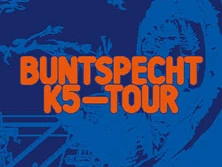 Blaue Fläche mit orangenem Schriftzug "Buntspecht K5-Tour" im grafisch stilisierten Hintergrund.