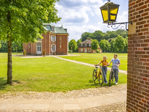Schloss Clemenswerth, Sögel – Radfahren Hümmling ©Emsland Tourismus GmbH (3).jpg Zwei Radfahrende spazieren auf dem Gelände von Schloss Clemenswerth bei sonnigem Wetter.