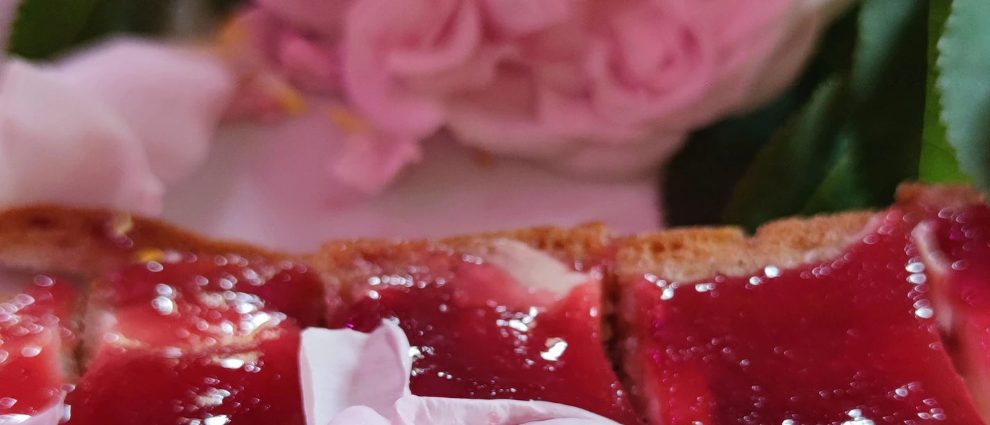 Rose kulinarisch Nahaufnahme eines Brotes mit roter Marmelade und rosa Blütenblättern darauf, im Hintergrund eine verschwommene rosa Blume.