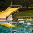 20010-FreibadRutsche_©GesUndTourismus Horn-Bad Meinberg GmbH.jpg Gelbe Rutsche im Freibad mit stufenlosem Zugang und spiegelndem Pool, umgeben von Bäumen und Grünflächen.