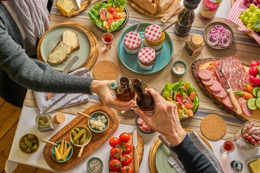 Gedeckter Tisch mit TYPISCH-neanderland Produkten und Ratuga Bier Einladender Tisch mit regionalen Produkten, Salaten und Ratuga Bier, Hände beim Anstoßen.