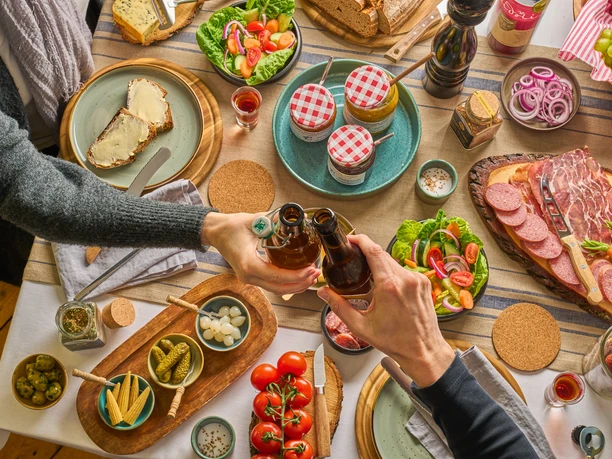 Gedeckter Tisch mit TYPISCH-neanderland Produkten und Ratuga Bier Einladender Tisch mit regionalen Produkten, Salaten und Ratuga Bier, Hände beim Anstoßen.