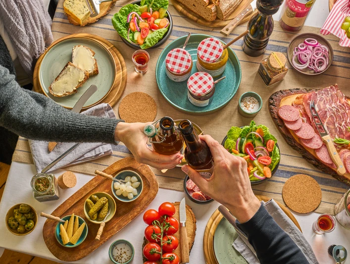 Gedeckter Tisch mit TYPISCH-neanderland Produkten und Ratuga Bier Einladender Tisch mit regionalen Produkten, Salaten und Ratuga Bier, Hände beim Anstoßen.