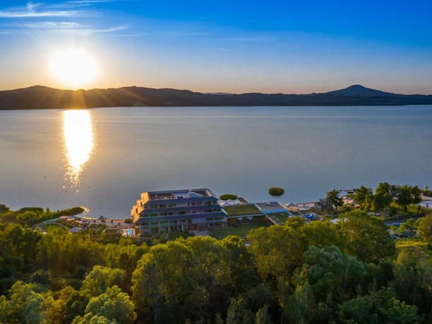 Sunset over a lake, in the foreground a modern building surrounded by trees.