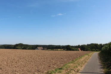 POI_1_Eschland.JPG Feldweg führt an weitläufigen Ackerflächen vorbei, im Hintergrund sind bewaldete Hügel zu sehen.