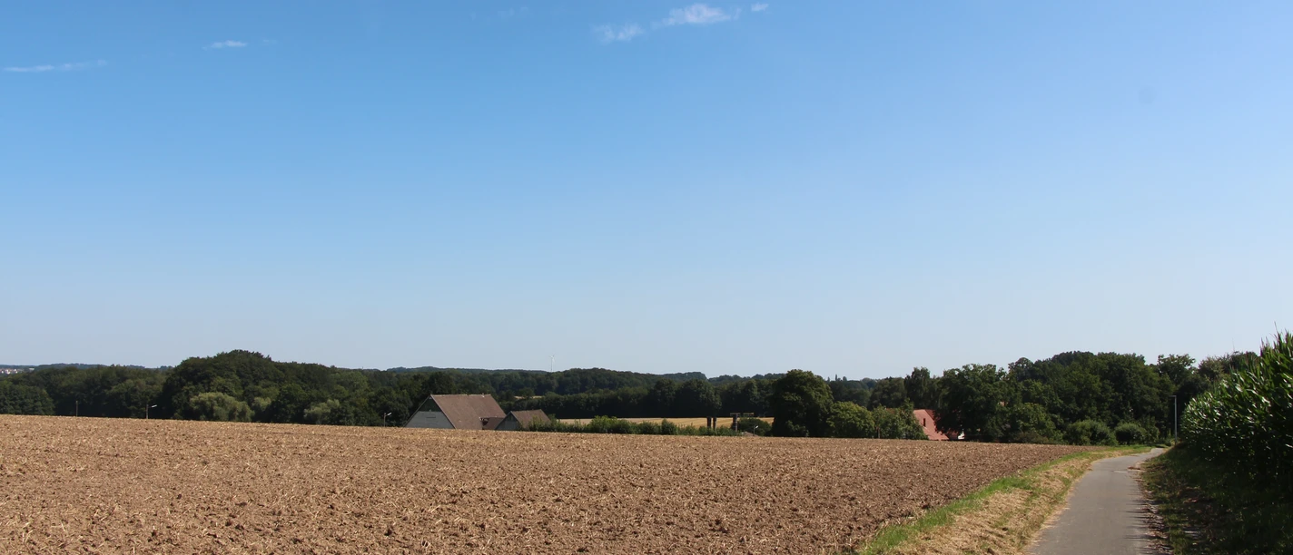 POI_1_Eschland.JPG Feldweg führt an weitläufigen Ackerflächen vorbei, im Hintergrund sind bewaldete Hügel zu sehen.