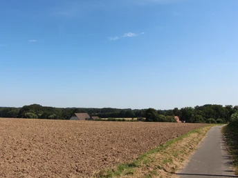 POI_1_Eschland.JPG Feldweg führt an weitläufigen Ackerflächen vorbei, im Hintergrund sind bewaldete Hügel zu sehen.