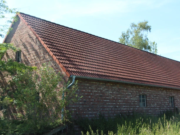 POI_2_Feldbrand_Haus.JPG Ehemaliges Feldbrandhaus mit ziegelgedecktem Satteldach, umgeben von wilder Vegetation.
