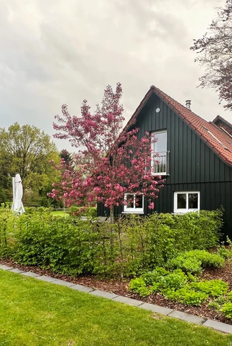 Das Bild zeigt eine alte, renovierte Schule mit dunkelgrüner Fassade, umrahmt von blühenden Bäumen.The picture shows an old, renovated school with a dark green façade, framed by blossoming trees.Billedet viser en gammel, renoveret skole med en mørkegrøn facade, indrammet af blomstrende træer.De foto toont een oude, gerenoveerde school met een donkergroene gevel, omringd door bloeiende bomen.