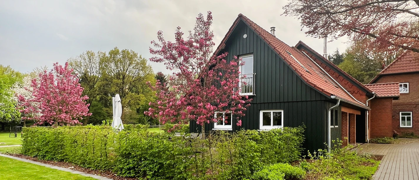 Alte Schule Kirchlinteln The picture shows an old, renovated school with a dark green façade, framed by blossoming trees.