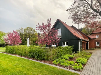 Alte Schule Kirchlinteln Das Bild zeigt eine alte, renovierte Schule mit dunkelgrüner Fassade, umrahmt von blühenden Bäumen.The picture shows an old, renovated school with a dark green façade, framed by blossoming trees.Billedet viser en gammel, renoveret skole med en mørkegrøn facade, indrammet af blomstrende træer.De foto toont een oude, gerenoveerde school met een donkergroene gevel, omringd door bloeiende bomen.