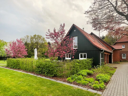 Alte Schule Kirchlinteln Das Bild zeigt eine alte, renovierte Schule mit dunkelgrüner Fassade, umrahmt von blühenden Bäumen.The picture shows an old, renovated school with a dark green façade, framed by blossoming trees.Billedet viser en gammel, renoveret skole med en mørkegrøn facade, indrammet af blomstrende træer.De foto toont een oude, gerenoveerde school met een donkergroene gevel, omringd door bloeiende bomen.