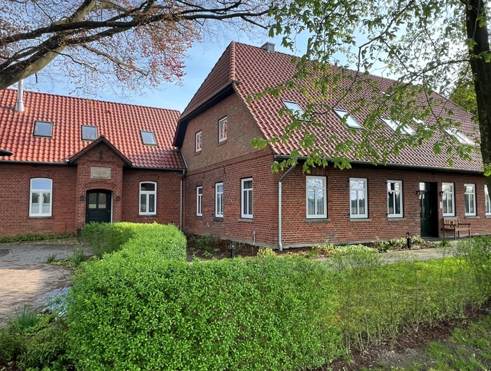 Alte Schule Kirchlinteln Backsteingebäude mit roten Dachziegeln und vielen Fenstern, umgeben von gepflegtem Grün und Bäumen.Brick building with red roof tiles and many windows, surrounded by well-tended greenery and trees.Murstensbygning med røde tagsten og mange vinduer, omgivet af velplejede grønne områder og træer.Bakstenen gebouw met rode dakpannen en veel ramen, omgeven door goed onderhouden groen en bomen.