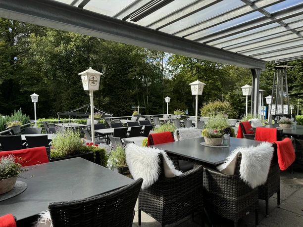 Außenterrasse - Ansicht Tropfsteinhöhle Gemütliche Terrasse eines Cafés mit überdachten Sitzbereichen, umgeben von grünen Bäumen.