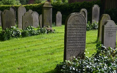 Jüdischer Friedhof Nordrehr Grabsteine mit hebräischer Schrift auf einem gepflegten Rasen, von Büschen umgeben. Ein Ort der Erinnerung.