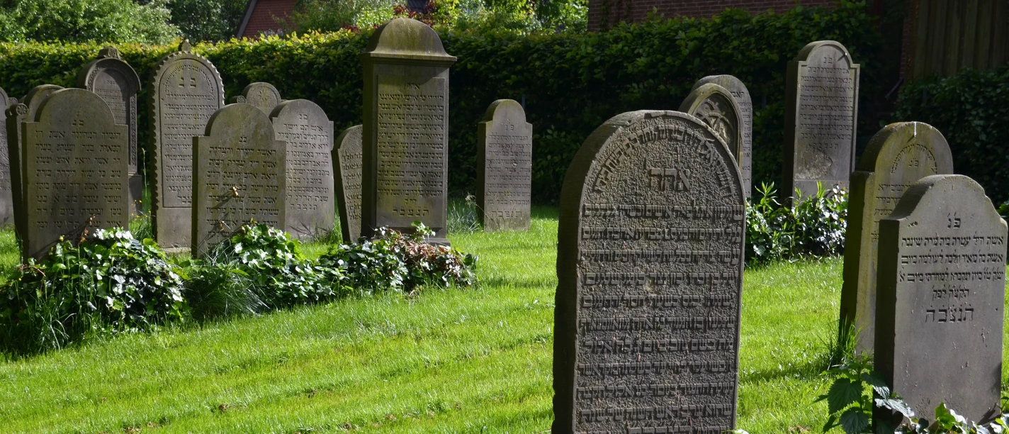 Jüdischer Friedhof Nordrehr Grabsteine mit hebräischer Schrift auf einem gepflegten Rasen, von Büschen umgeben. Ein Ort der Erinnerung.