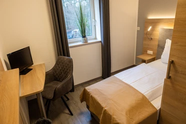 Balkes Morhoff_Zimmer Einzelzimmer mit modernem Design, Schreibtisch, komfortablem Stuhl und Blick auf bewaldete Umgebung.