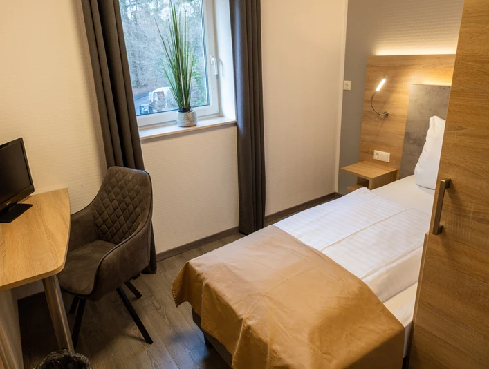 Balkes Morhoff_Zimmer Einzelzimmer mit modernem Design, Schreibtisch, komfortablem Stuhl und Blick auf bewaldete Umgebung.