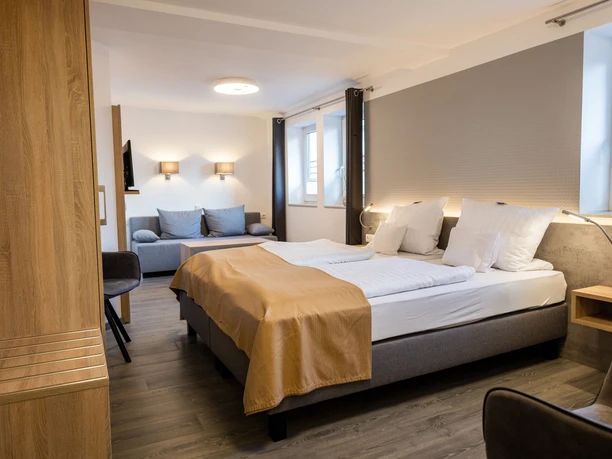 Balkes Morhoff_Zimmer Doppelzimmer mit Doppelbett, heller Einrichtung, Sofa und Schreibtisch, Ausblick aus großen Fenstern.