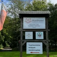 Schild - Waldhotel Tropfsteinhöhle Waldhotel-Schild mit Angeboten wie Restaurant, Kegelbahn und Sauna vor grünen Bäumen und Flaggen.