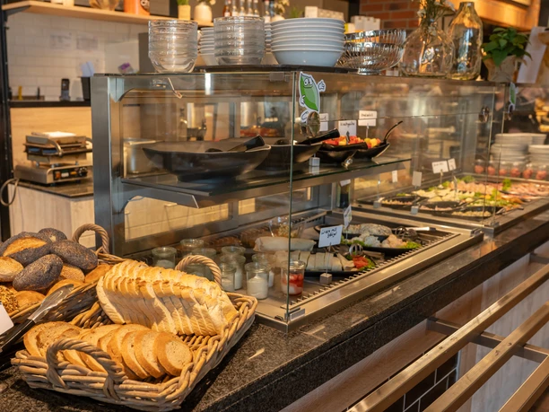 Ferdinands Bäckerei | Restaurant Brotauswahl vor einem Buffet mit frischen Brötchen, Brot, Müsli-Gläsern und Wurstplatten.