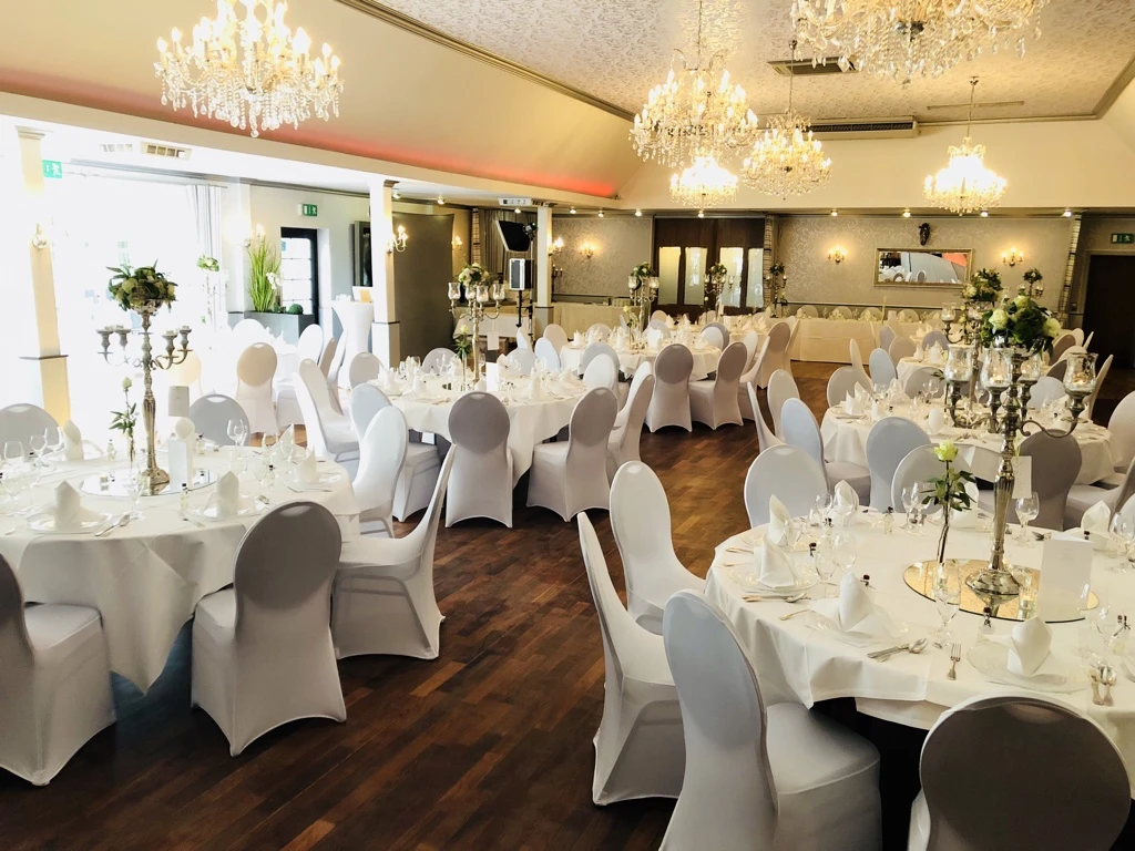 Balkes Morhoff Eleganter Festsaal mit runden Tischen, weißen Tischdecken und Kronleuchtern. Einladend dekoriert.