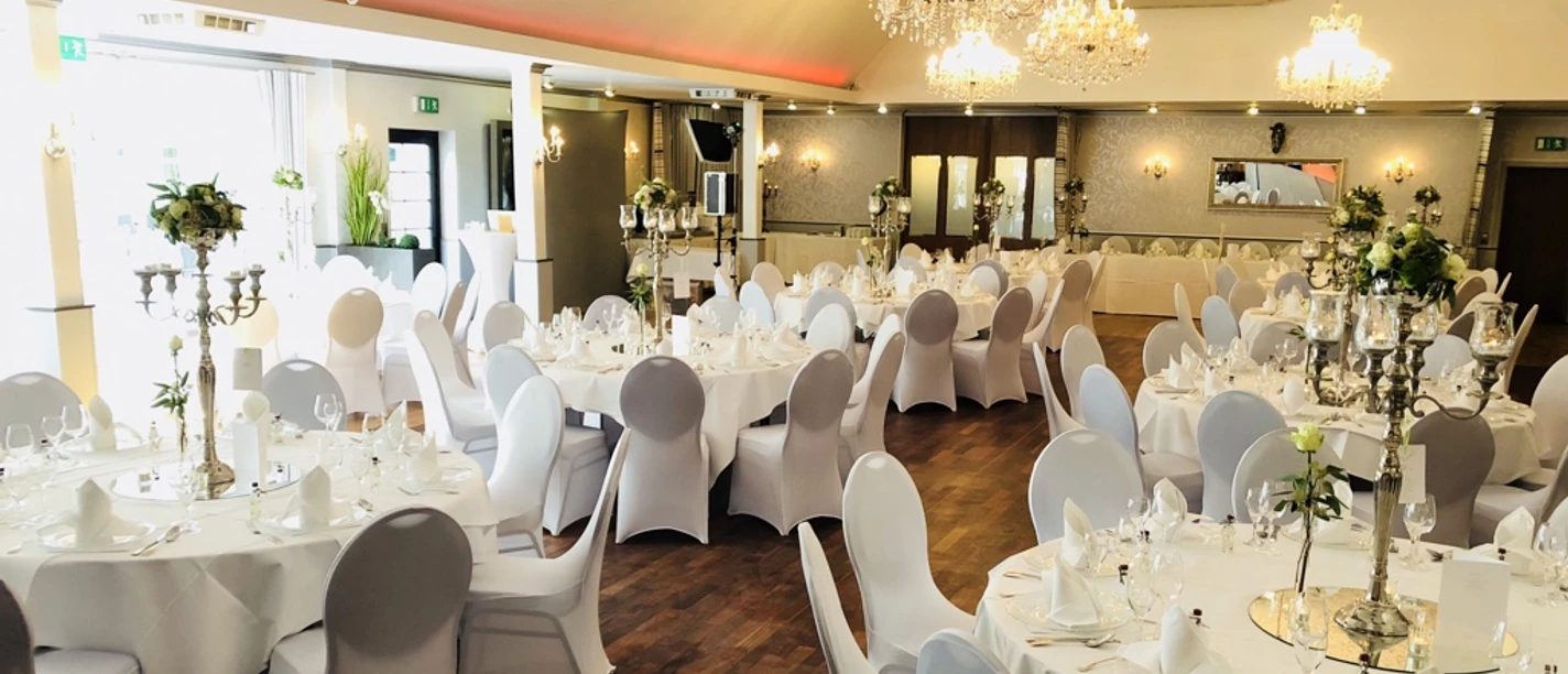 Balkes Morhoff Eleganter Festsaal mit runden Tischen, weißen Tischdecken und Kronleuchtern. Einladend dekoriert.