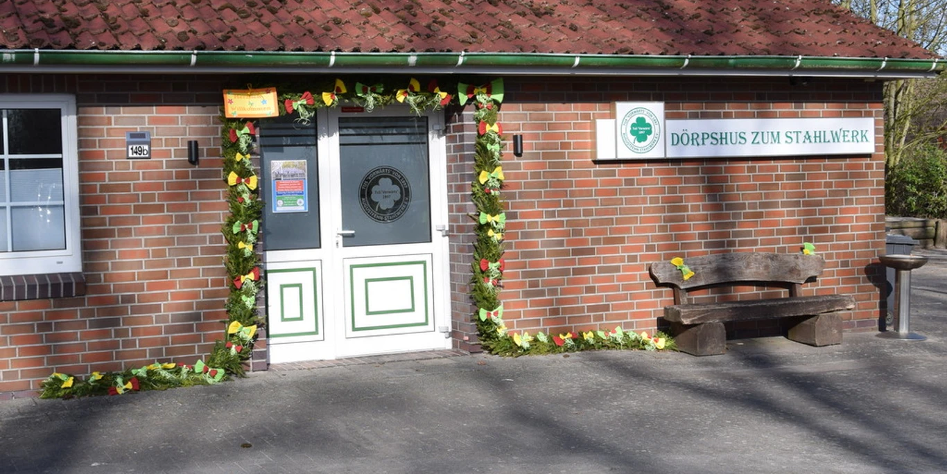 Dörpshus zum Stahlwerk.jpg Zu sehen ist das Dörpshus zum Stahlwerk mit einer einladenden Eingangstür, umrahmt von buntem Laub.