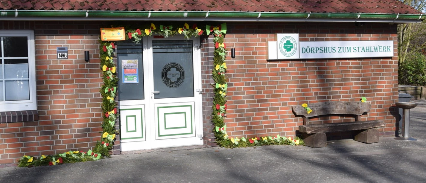Dörpshus zum Stahlwerk.jpg Zu sehen ist das Dörpshus zum Stahlwerk mit einer einladenden Eingangstür, umrahmt von buntem Laub.