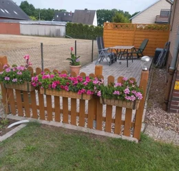 Ferienwohnung Angelmann Ferienwohnung Angelmann: Holzterrasse mit Blumen, Gartenideen und Sitzbereich, umgeben von Zäunen.