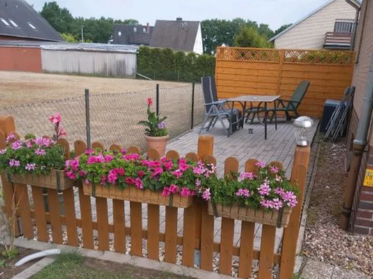 Ferienwohnung Angelmann Ferienwohnung Angelmann: Holzterrasse mit Blumen, Gartenideen und Sitzbereich, umgeben von Zäunen.