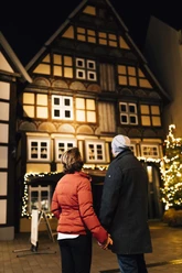 Ein Paar steht bei Nacht vor einem historischen Fachwerkhaus. Die Umgebung ist festlich mit Lichtern geschmückt.
