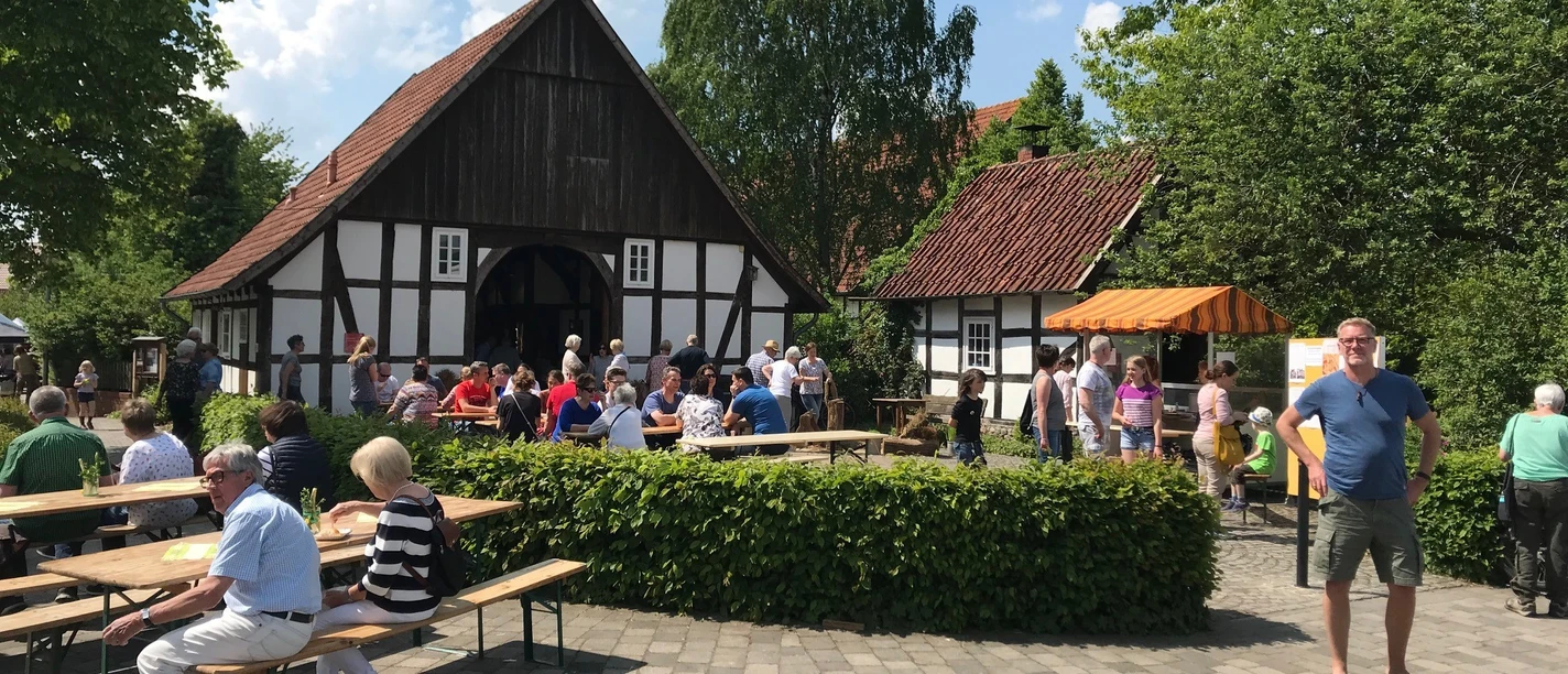Vor_dem_Kotten_Jutta_Redecker.jpg Eine Gruppe von Menschen genießt eine sonnige Veranstaltung vor einem Fachwerkhaus mit Baum.