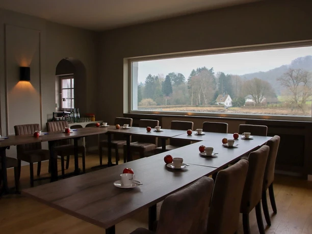 Haus am See (4).jpg Seminarraum mit Stühlen und Tischen in U-Form auf denen Kaffeetassen und Äpfel liegen. An der Wand ist ein langes Fenster.