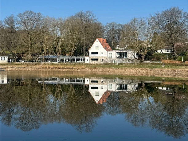 Haus mit Außenbereich an einem See, das sich zusammen mit den Bäumen im Wasser spiegelt