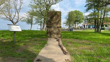 Steinhude sculpture promenade: Upright stone slab with chains on a meadow on the lakeshore.