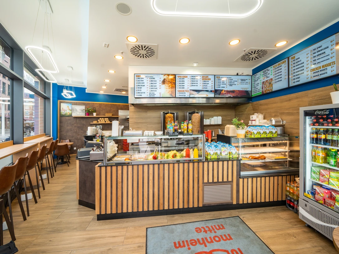 Dönerstation 789 Ein einladender Imbissladen mit Theke, Speisekarte an der Wand, Sitzmöglichkeiten und Kühlschrank.