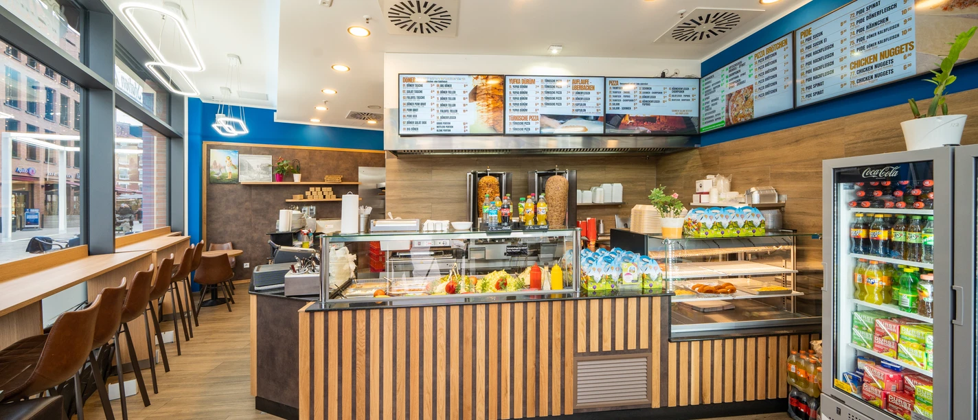 Dönerstation 789 Ein einladender Imbissladen mit Theke, Speisekarte an der Wand, Sitzmöglichkeiten und Kühlschrank.