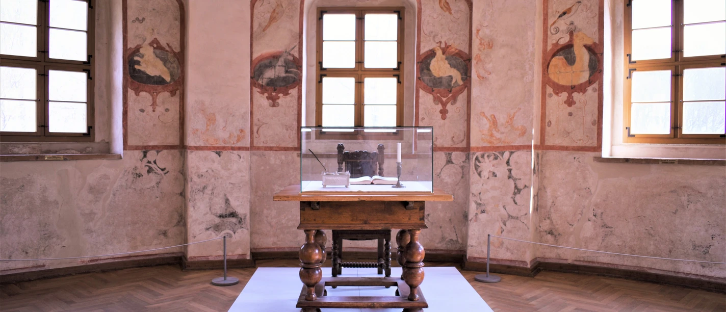 03-KSC-Burg Rabenstein_Tafelstube.JPG Raum in Burg Rabenstein mit mittelalterlicher Dekoration und einem Tisch unter Glasvitrine.