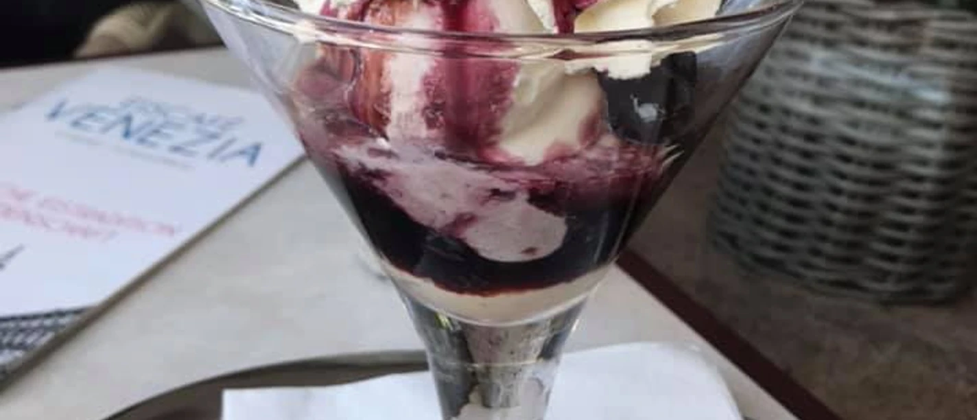 Ein eleganter Eisbecher mit Sahne, Fruchtsauce und Waffel im Eiscafé Venezia auf einem Tablett serviert.