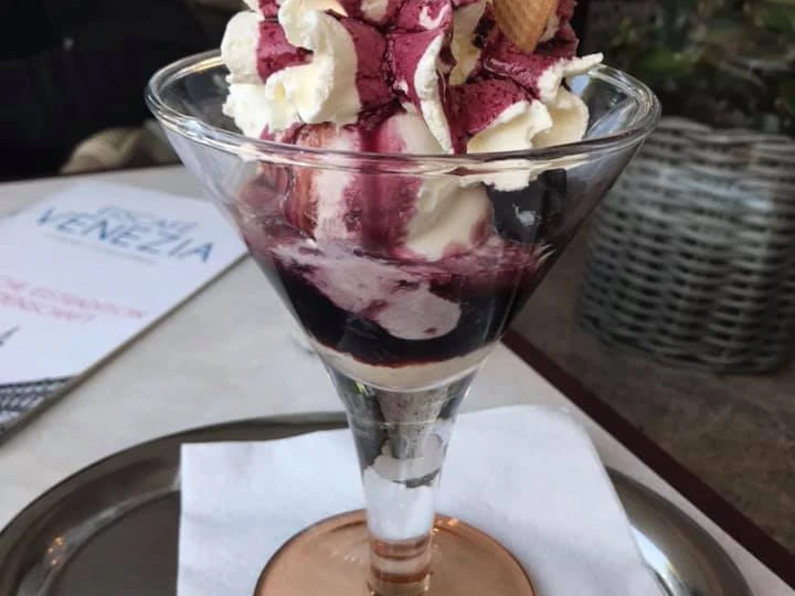 Ein eleganter Eisbecher mit Sahne, Fruchtsauce und Waffel im Eiscafé Venezia auf einem Tablett serviert.