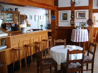 Gemütliche Gaststube mit Holzmöbeln, Bartresen und dekorativen Bildern an der Wand.