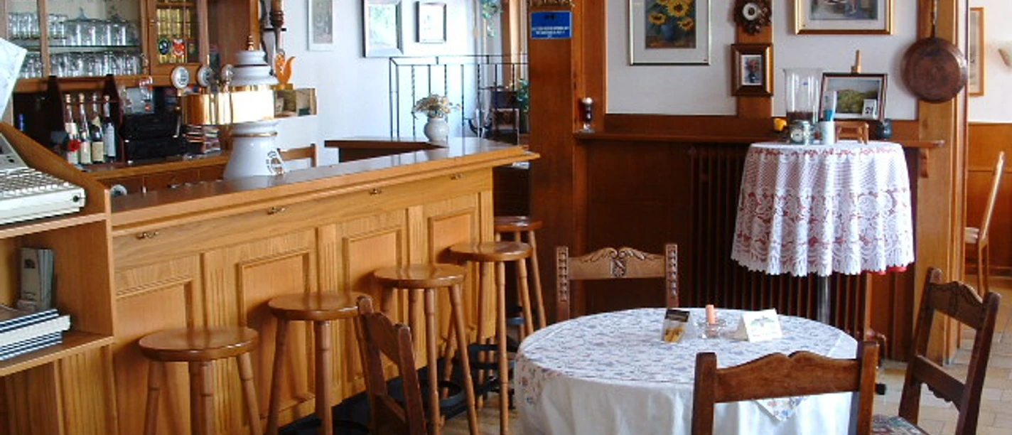 Gaststube (1).JPG Gemütliche Gaststube mit Holzmöbeln, Bartresen und dekorativen Bildern an der Wand.