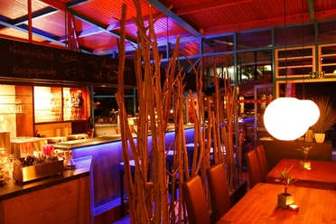 Ein stilvoll beleuchteter Barbereich mit farbigem Licht, modernen Holzmöbeln und dekorativen Zweigen.